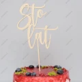 Drewniany topper na tort „Sto Lat” wbitę w czerwony tort z owocami.