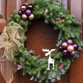 Świąteczny wieniec z gałązek świerku, ozdobiony złotymi kokardami i fioletowymi bombkami. W centrum znajduje się drewniany renifer.