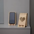 Dwa drewniane stojaki na telefon - serce geometryczne, z telefonami, jeden z wyciętym sercem, drugi z telefonem w środku, na szarym tle.