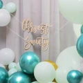 Girlanda drewniana Chrzest Święty zawieszona na tle balonów w odcieniach bieli i turkusu.