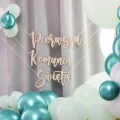 Girlanda drewniana Pierwsza Komunia Święta z literami na tle balonów w kolorach bieli i zieleni.