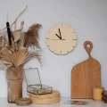 Zegar ze sklejki brzozowej z czarnymi wskazówkami, widoczny na tle dekoracji w stylu boho.
