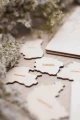 Drewniane puzzle - mapa Polski, widok na elementy z nazwami województw, ułożone na drewnianej powierzchni, w tle dekoracja.