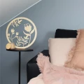 Drewniane kwiaty na łodyżkach w okrągłej ramie, ozdoba ze sklejki brzozowej na czarnym stoliku obok sofy z poduszkami.