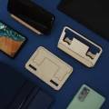Kompaktowy stojak na telefon z drewna w kilku wariantach, z telefonami komórkowymi na niebieskim tle.