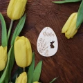 Personalizowana zawieszka na Wielkanoc z imieniem Natalia, w kształcie jaja z grawerem z zajączkiem i kwiatami, na tle tulipanów.