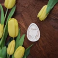 Personalizowana zawieszka wielkanocna w kształcie jajka z imieniem Natalia i uszami zajączka, obok żółtych tulipanów.