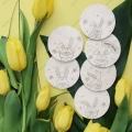 Podkładki pod kubek z zajączkami ze sklejki brzozowej ułożone na liściu i tle z żółtymi tulipanami, widok z góry.